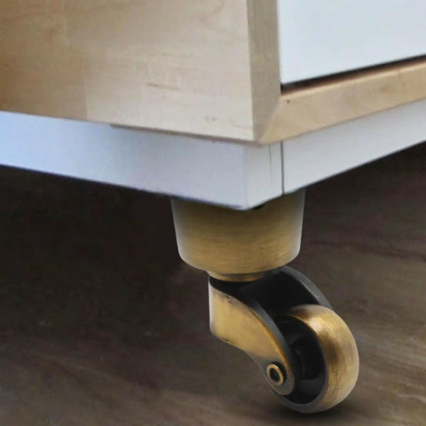 Four Piece Antique Brass Furniture Casters Crafted From Solid Cast Zinc Alloy featuring smooth 360 degree swivel rollers under a cabinet.
