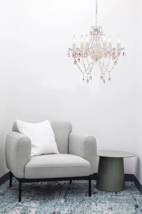 White Crystal Chandelier With Pink Droplets And Strands 6 Light Candle Style Ceiling Fixture For Bedroom Or Dining Vintage Glam Lighting With Elegant Scroll Arm Frame in a modern room with gray chair