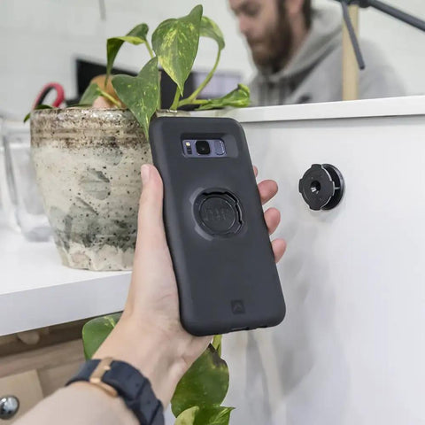 Hand holding phone case near Adhesive Phone Wall Mount Twin Pack For Non Porous Surfaces With 3M VHB Backing Sticks To Any Case Or Universal Adapters No Fuss Easy Permanent Wall Mount Or Screw In Option For A Clean Setup on wall.