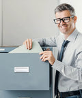 Smiling man in glasses using a gray filing cabinet in an office setting