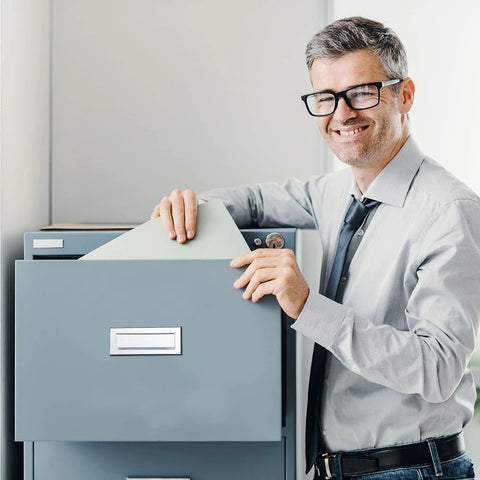 Smiling man in glasses using a gray filing cabinet in an office setting