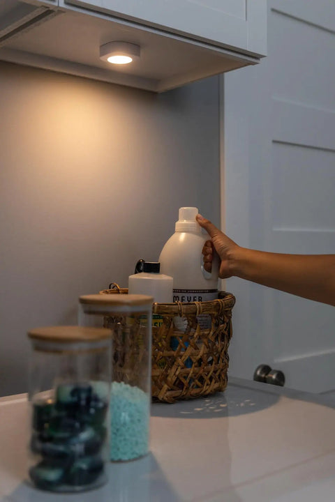 Tap On Off LED Light Stick-On Battery Powered Wireless Portable Light illuminating a cabinet with baskets and jars below