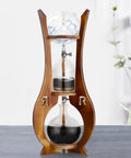 Skip The Store Bought Stuff And Sip Dope Flavor With This Portable Cold Brew Drip Tower Featuring Dual Adjustable Valves High Borosilicate Glass Large Capacity For Bold Iced Coffee in wooden stand with ice and brewing coffee.