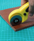45mm Rotary Cutter Kit With 9 Replacement Blades cutting leather on a green cutting mat