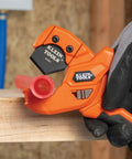 Lightweight PEX Pipe And Tubing Cutter with soft molded handles and pierce point blade cutting red PEX tubing on wood surface.