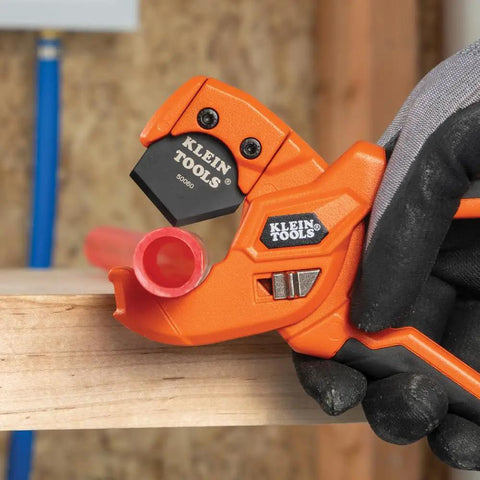 Lightweight PEX Pipe And Tubing Cutter with soft molded handles and pierce point blade cutting red PEX tubing on wood surface.