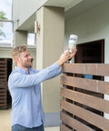 Man installing Ws90 7 In 1 Outdoor Weather Station With Bluetooth And Zigbee Connectivity on a wooden fence outside house