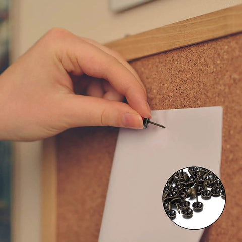 Hand using 250 Piece Hand Forged Bronze Upholstery Tacks For Furniture And Sofas to pin paper on a cork board.