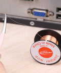 Tweezers holding a strand of the 0.1mm 5Pcs Ultra Thin Soldering Wire Set Copper Jumper Wires For PCB Repair Mobile Phone And Computer Electronics Precision Flexible Link Jump Wires Pro Grade DIY Welding Tools with a spool visible in the background.