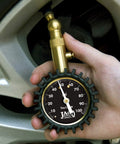 Close-up of brass JACO Elite tire pressure gauge with a 0–100 psi dial held near a tire valve.