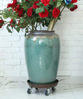 Big Boy Rolling Plant Dolly With Lockable Casters For Smooth Riding Indoors Or Outdoors, Built Like A Tank At Four Hundred Twenty Lb Capacity, Thickened Steel Pan With No Cutouts, Fits Twelve To Fifteen Inch Pots, Pack Of Two supporting a large ceramic pot filled with flowers.