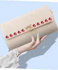 Front view: beige clutch purse with red circular rivet studs along the top edge and a gold clasp, held by a hand.