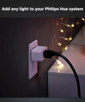 Hue Smart Plug Turns Any Lamp Into a Smart Light with no fuss, plugged into a wall outlet with lights in the background.