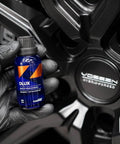 CARPRO DLUX wheel and trim coat bottle (blue) held by gloved hand beside a car wheel