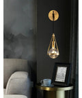 Slick Premium Copper LED Wall Sconce Featuring Glare Free Crystal Shade For Modern Bedroom Bedside Hallway And Staircase Decor With Tight Rust Proof Build And Killer Warm Ambient Glow mounted beside a modern gray sofa.
