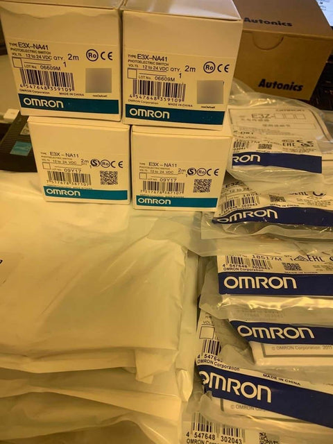 Stack of Omron E3X-NA41 photoelectric sensors with packaging, ideal for automation lines, featuring precise sensing with fiber optic cable.