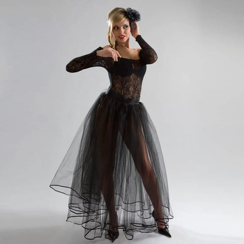 Woman in elegant black tulle gown with lace top and long sleeves, accessorized with a hairpiece, standing against gray background.
