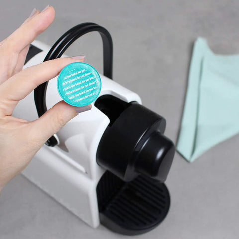 Hand holding a cleaning capsule in front of a Nespresso machine, part of the Nespresso Original Machines Cleaning Pods Set.