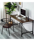 Slick Rolling Computer Desk Featuring Tight Vintage Industrial Lines And A Roomy Wood Surface Built For Home Office Setups With Heavy Duty Metal Base And Smooth Glide Casters, shown with a plant and workspace.