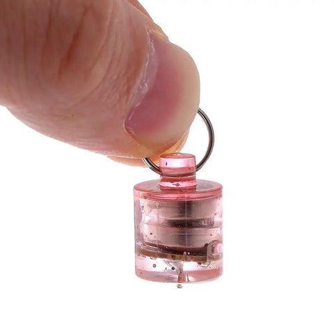 Close-up of a hand holding a small pink LED fishing light from the 5 Pack LED Fishing Lights For Deep Water Drops, Underwater Round Squid Strobe Bait Lure