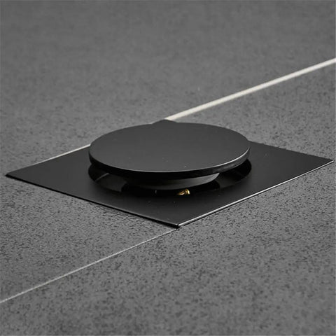 Drop Down Square Pop Up Floor Drain With Matte Black Chrome Cap and Odor Locking Grille For Bathrooms on textured tile floor.