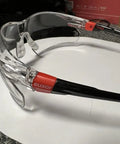 Side view of lightweight safety glasses with adjustable arms and soft nose pad, ANSI Z87 EN 166 certified, on a surface.