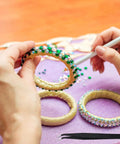 Hands using Bedazzler Kit With Rhinestones And Hot Fix Gems Craft Applicator on bangle with diamond painting pen and tweezers visible