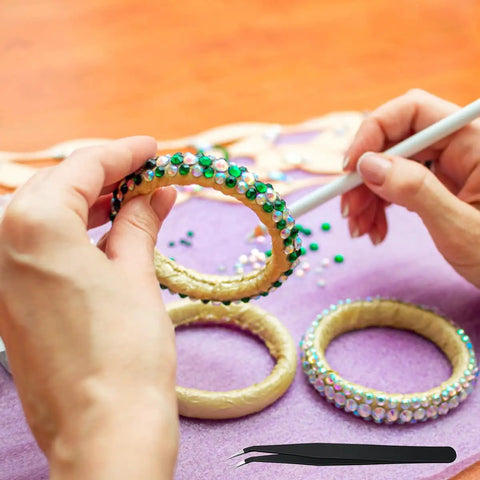 Hands using Bedazzler Kit With Rhinestones And Hot Fix Gems Craft Applicator on bangle with diamond painting pen and tweezers visible