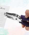 Hand using 16 Pack Handheld Hole Puncher With Soft Grip 1/4 Inch Circle Punch on greeting card, featuring purple grip