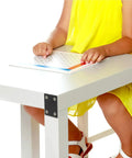 Child using a white table with black stainless steel mending plates for stability, holding a book.