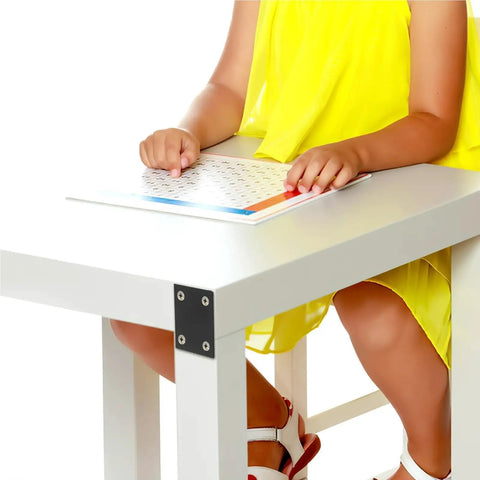 Child using a white table with black stainless steel mending plates for stability, holding a book.