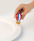 Hand placing Red White Balloon Hand Painted Ceramic Holiday Decor Spring Mini on a white tabletop for home and office use.
