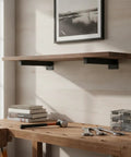 Multipurpose Black Steel Shelf Brackets For Garage, Kitchen And Workshop holding wooden shelf above workbench with tools and books.