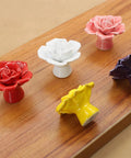 Colorful rose flower ceramic knobs on wooden board, displaying red, white, pink, yellow, and purple variations for cabinetry and dresser decor.