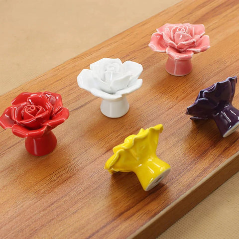 Colorful rose flower ceramic knobs on wooden board, displaying red, white, pink, yellow, and purple variations for cabinetry and dresser decor.