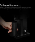 Hand holding container near Badass Electric Coffee Grinder With 150 Tight Adjustments, Slick Stainless Steel Housing, And Knockout Uniform Grind For Espresso Pour Over And French Press In Matte Black.