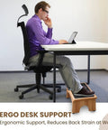 Man using a 7-inch wooden under desk adjustable foot rest with three level incline for ergonomic support at office desk.