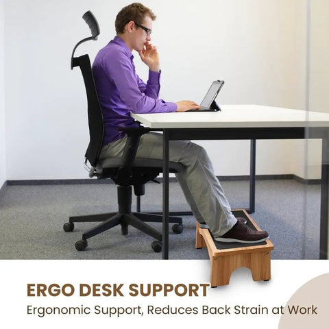 Man using a 7-inch wooden under desk adjustable foot rest with three level incline for ergonomic support at office desk.