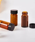 15 Piece Kit Of 10Ml Amber Glass Sample Vials With Black Screw Caps And Pe Liners, 0.34 Oz Tiny Travel Flasks For Essential Oils Perfume Lab Reagents Zero Sweat Spills Badass Reliable Build - three vials standing upright on a white surface.