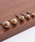 Close-up of five 20-Piece Pack Antique Brass Upholstery Tacks on wood, showing different sizes and threaded steel bodies.