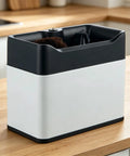 Automatic Electric Portafilter Cleaner For Coffee Grounds with black top, white base, and brush inside on wooden counter.