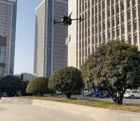 Dual Payload Drop Kit With Emergency Lighting For M30 Drone flying near skyscrapers, visible in clear urban sky with trees.
