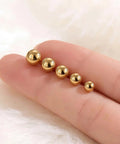 Five Piece Gold Ball Stud Earrings Set For Women Including 3mm 4mm 5mm 6mm And 7mm Sizes, 14K Gold Plated With 316L Steel Pins, Super Versatile Everyday Earrings. Five gold ball studs in mixed sizes on a finger