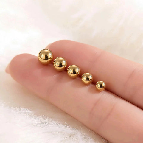 Five Piece Gold Ball Stud Earrings Set For Women Including 3mm 4mm 5mm 6mm And 7mm Sizes, 14K Gold Plated With 316L Steel Pins, Super Versatile Everyday Earrings. Five gold ball studs in mixed sizes on a finger