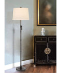 Three Way 150W Riverwood Metal Floor Lamp With Adjustable Height And Weighted Base Featuring A Sturdy Hardback Tapered Fabric Drum Shade In Silver Finish next to a cabinet.
