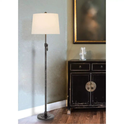 Three Way 150W Riverwood Metal Floor Lamp With Adjustable Height And Weighted Base Featuring A Sturdy Hardback Tapered Fabric Drum Shade In Silver Finish next to a cabinet.