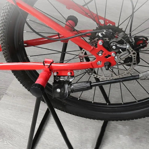 Close-up of a beefy heavy duty folding bike stand securing a red mountain bike, showing 360 degree clamp and aluminum frame for maintenance.