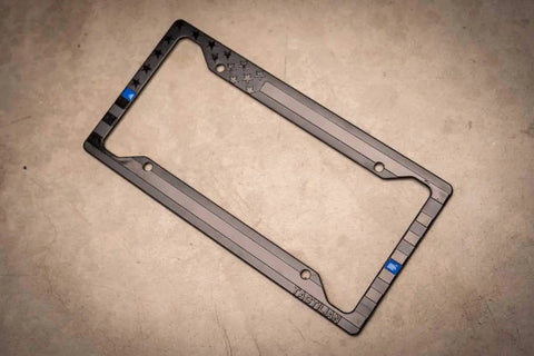 Subdued 3D Embossed American Flag License Plate Frame with Black Gloss on Matte Finish, featuring Thin Blue Line, angled view