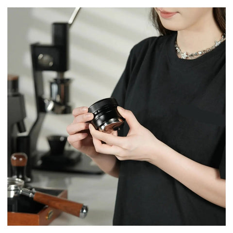 Pro Level Espresso Coffee Distributor And Tamper Set 58.35mm in hand, showcasing gravity adaptive black stainless steel design.
