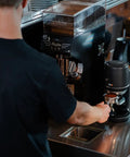 Electric Auto Leveling Espresso Tamper For 57.3 Mm Portafilters in use at a coffee counter with grinder and espresso machine